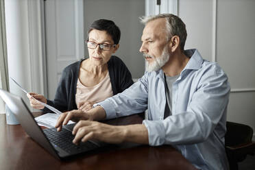 Älteres Ehepaar spricht über Familienangelegenheiten, während es zu Hause am Tisch vor einem Laptop sitzt - KPEF00364