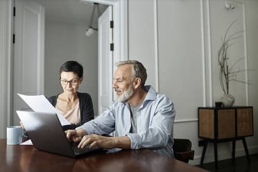Couple discussing business paper sitting in front of laptop - KPEF00365