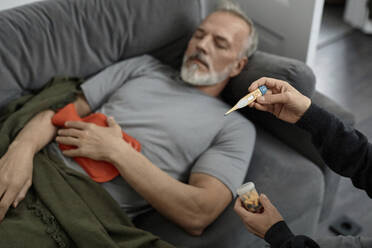 Unbekannte Frau schaut auf das Thermometer, während sie zu Hause neben ihrem kranken Mann sitzt - KPEF00367