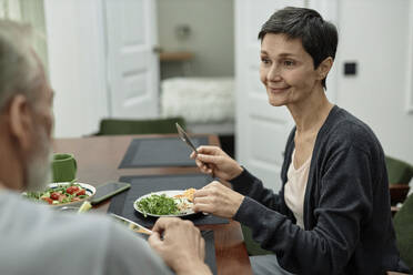 Erwachsene Frau sieht ihren Mann an, während sie Spiegeleier und Salat isst - KPEF00373