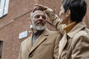 Woman fixing her husbands hair while walking at street - KPEF00383