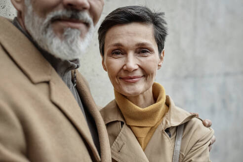 Adult woman looking at camera standing next to her husband with gray beard outdoors - KPEF00396