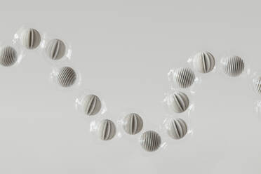3D-Rendering einer Reihe von in Plastik eingewickelten Kugeln, die vor einem weißen Hintergrund schweben - GCAF00493