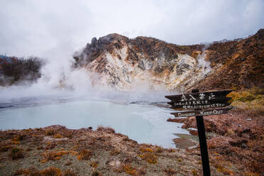 Gefahrenschild vor einem vulkanischen Feld und einem dampfenden Teich in Noboribetsu, Höllental, Hokkaido, Japan, Asien - RHPLF29478