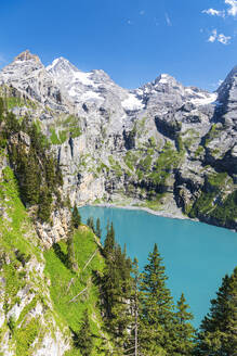 Elevated view of the crystal blue water of the lake of Oeschinensee among pine trees and alpine peaks covered with snow, Oeschinensee, Kandersteg, Bern Canton, Switzerland, Europe - RHPLF29845