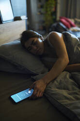 Junge Frau schaltet den Wecker auf dem Smartphone zu Hause aus - DSHF01117