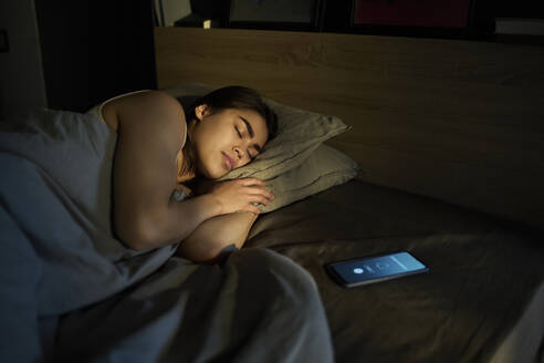 Woman sleeping near alarm ringing on smart phone at home - DSHF01119