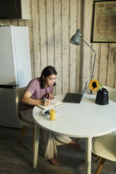 Young student preparing notes with laptop at table - DSHF01140