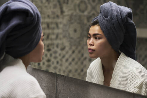 Junge Frau trägt ein Handtuch auf dem Kopf und schaut in den Spiegel zu Hause - DSHF01154