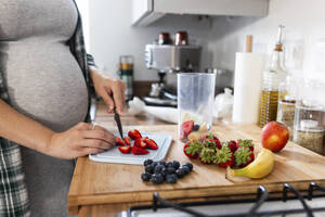Schwangere Frau schneidet in der Küche Erdbeeren für einen Milchshake - WPEF07853