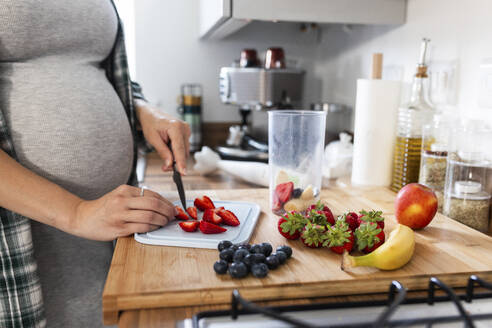 Pregnant woman chopping strawberries for milkshake in kitchen - WPEF07853