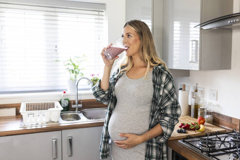 Schwangere Frau trinkt Milchshake in der Küche zu Hause - WPEF07860
