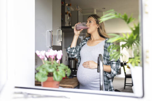 Schwangere Frau trinkt Milchshake durch Fenster gesehen - WPEF07861