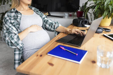 Schwangere Freiberuflerin arbeitet am Laptop im Home Office - WPEF07863