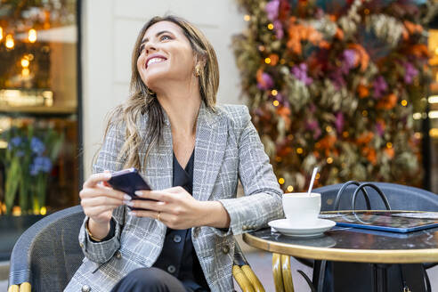 Glückliche Geschäftsfrau mit Smartphone in einem Straßencafé - DLTSF03678