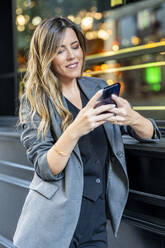 Geschäftsfrau mit Smartphone in der Nähe der Wand stehend - DLTSF03684