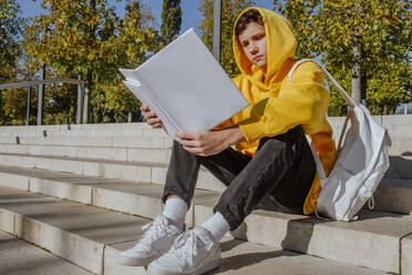 Studentin sitzt auf den Stufen und liest ein Buch im Park - MDOF01724