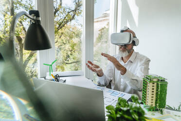 Architect wearing Virtual reality simulators gesturing at desk - YTF01433