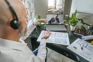 Smiling architect discussing on video call with colleague through laptop at desk - YTF01437