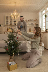 Lächelnde Frau beim Schmücken des Weihnachtsbaums mit einem Mann, der zu Hause steht - VPIF08951