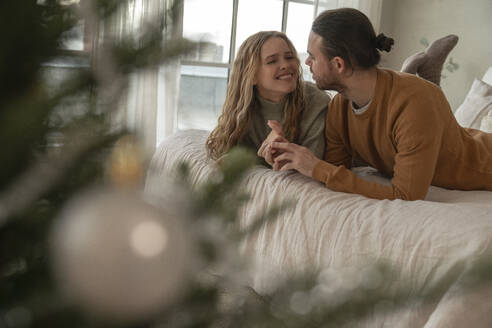 Lächelndes Paar auf dem Bett liegend in der Nähe des Weihnachtsbaums zu Hause - VPIF08965