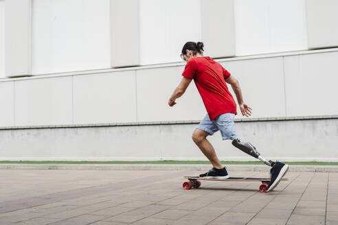 Junger Mann mit Beinprothese fährt Skateboard auf dem Gehweg - JCZF01289