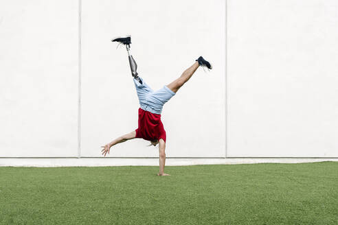Young man with prosthetic leg doing handstand in front of wall - JCZF01295