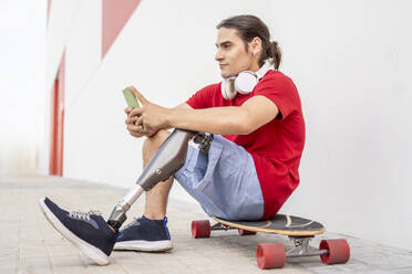 Nachdenklicher Mann mit Behinderung sitzt auf einem Skateboard - JCZF01310