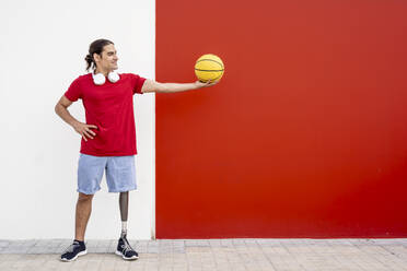 Glücklicher Mann mit Beinprothese hält gelben Basketball an der Wand - JCZF01318