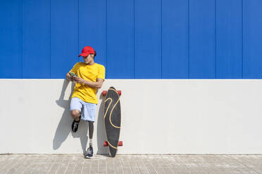 Mann mit Behinderung benutzt Smartphone in der Nähe des Skateboards an einem sonnigen Tag - JCZF01328