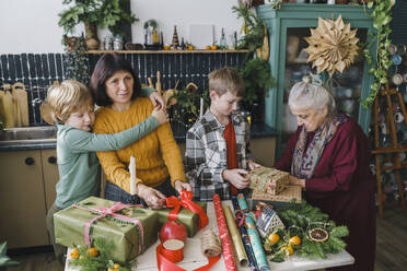 Familie hilft sich gegenseitig beim Verpacken von Weihnachtsgeschenken zu Hause - VBUF00513