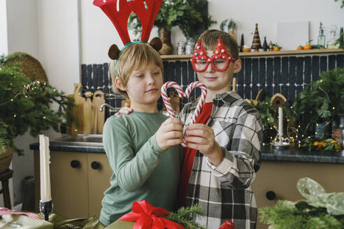 Brothers making heart shape from candy cane in kitchen at home - VBUF00524