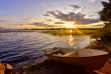 Sweden, Gavleborg County, Hedesunda, Empty rowboat lying on Lakeshore at sunset - FDF00409