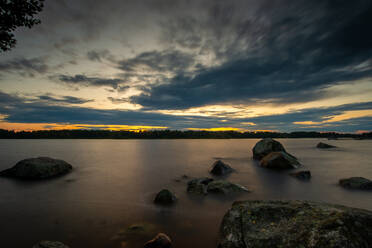 Sweden, Gavleborg County, Hedesunda, Clouds over lakeshore boulders at dusk - FDF00411