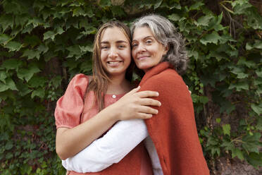 Happy mother hugging pregnant daughter near plants - AAZF01359