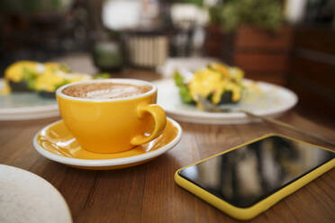 Yellow coffee cup with smart phone on table at cafe - AAZF01378