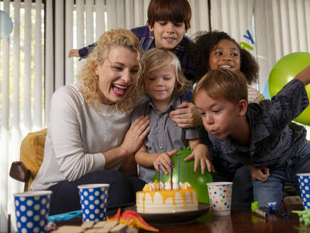 Boy blowing birthday candles with mother and friends at home - IKF01429