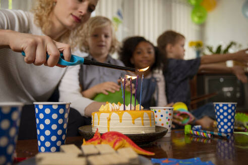 Woman lighting candles on birthday cake at home - IKF01431