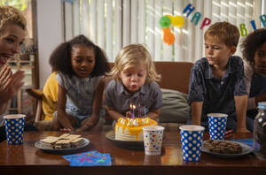 Junge bläst Kerzen auf seinem Geburtstagskuchen aus, während seine Freunde zusehen - IKF01433