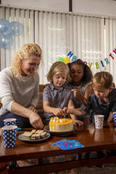 Boy celebrating birthday with mother and friends at home - IKF01434