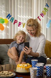 Birthday boy with mother talking on video call at home - IKF01437