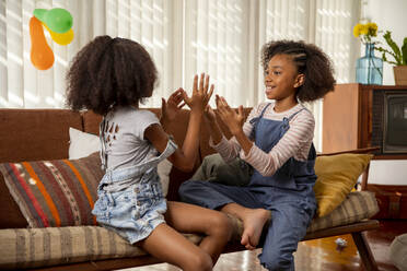 Glückliche Mädchen spielen Klatschspiel auf dem Sofa zu Hause - IKF01445