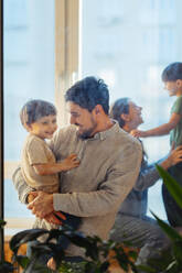 Father carrying son in arms with family at home - ANAF02467