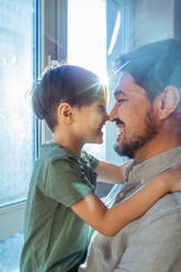 Liebevoller Vater und Sohn reiben sich zu Hause am Fenster die Nasen - ANAF02470