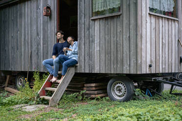 Lächelndes Paar sitzt in der Tür einer Blockhütte - JOSEF22155