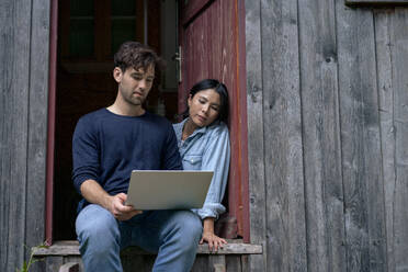 Freelancer working on laptop with woman sitting in doorway - JOSEF22185