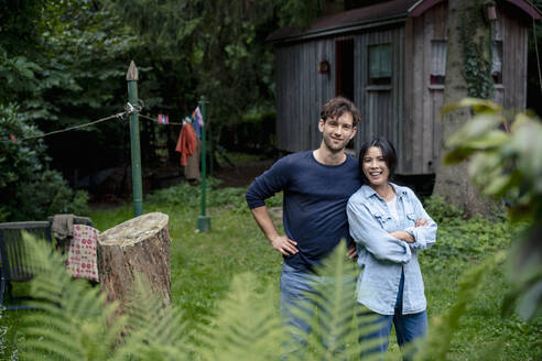 Smiling man standing with woman in front of log cabin - JOSEF22202