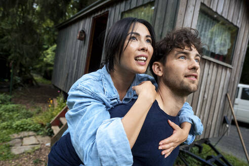 Happy man giving piggyback ride near log cabin - JOSEF22209