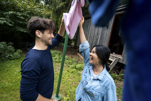 Glücklicher Mann und Frau mit rosa Tuch zum Trocknen vor einer Blockhütte - JOSEF22213