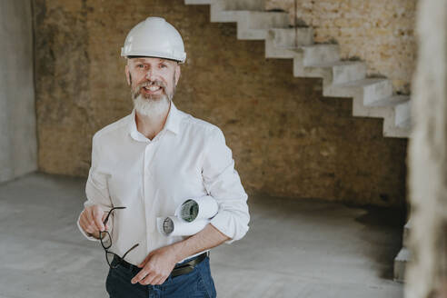 Happy mature architect standing at construction site - YTF01450